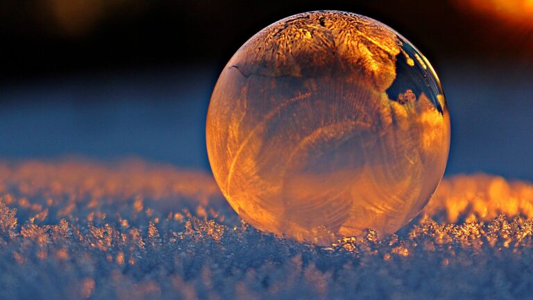 Close-up shot of a frozen bubble with warm reflections resting on a snowy surface at twilight.